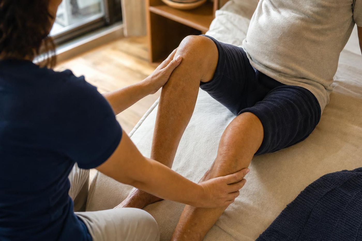 Mãos de fisioterapeuta orientando um exercício de joelho, em casa